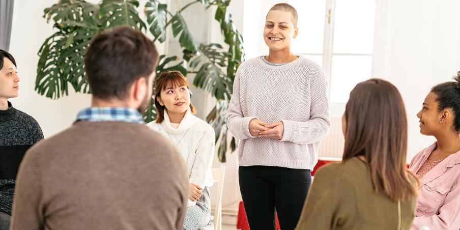 Eine Frau steht lächelnd in einem Kreis von Menschen auf Stühlen