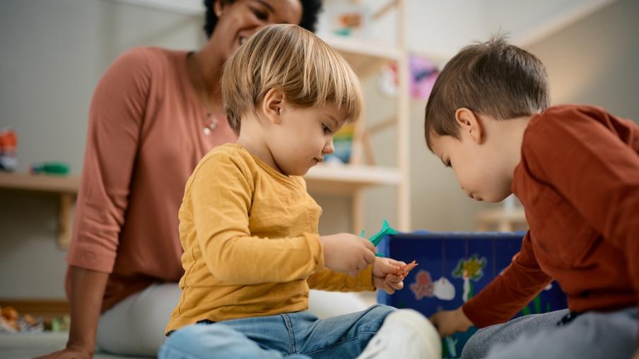 
		Zwei Kleinkinder spielen und Betreuungsperson schaut zu
	